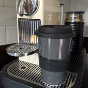 Charcoal coloured reusable travel mug on a coffee machine.