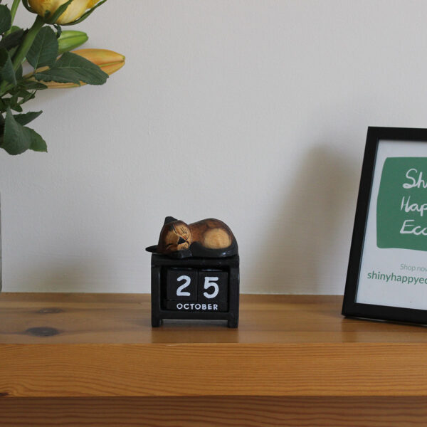Front view of sleeping cat block calendar in dark brown on black pictured on a mantlepiece.